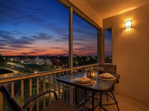 Un balcon avec une table dressée pour deux personnes, donnant sur un quartier résidentiel au crépuscule.