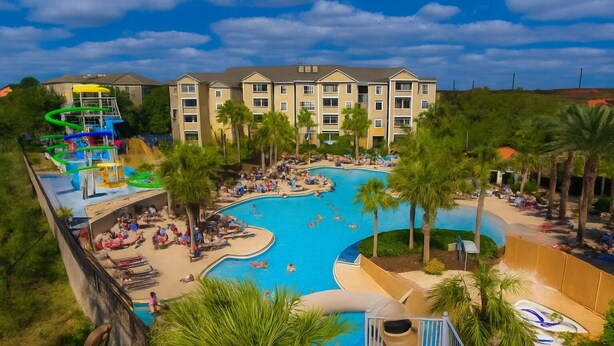 A resort with a large pool, palm trees, and a water slide. - 3BR Updated Windsor Hills condo Near Disney + Water Park! (Kissimmee)