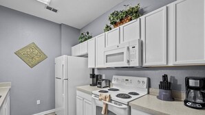 A modern kitchen with white cabinets, a built-in microwave, a stove, and a coffee maker. - 3BR Updated Windsor Hills condo Near Disney + Water Park! (Kissimmee)