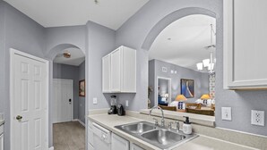 A modern kitchen with white cabinets, a double sink, and a countertop with a coffee maker and blender. - 3BR Updated Windsor Hills condo Near Disney + Water Park! (Kissimmee)