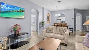 A spacious living room with a large TV, a ceiling fan, and a wooden coffee table. - 3BR Updated Windsor Hills condo Near Disney + Water Park! (Kissimmee)