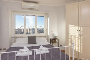 A bedroom with a bed, a window, an air conditioner, a bedside table with a lamp, and a wardrobe. - Rental in Rome Pyramid View Apartment (Rome)