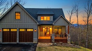 Une maison à deux étages avec un porche à l’avant, des fondations en pierre et un garage à deux portes.