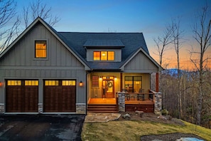 Une maison à deux étages avec un porche à l’avant, des fondations en pierre et un garage à deux portes.
