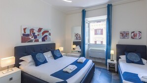 A hotel room with two beds, a large window with curtains, artwork on the walls, and a modern light fixture. - Rental in Rome Principe Amedeo Apartment (Rome)