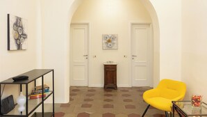 A hallway with an arched ceiling, a small wooden cabinet, a yellow chair, and a glass table with a vase. - Rental in Rome Principe Amedeo Apartment (Rome)