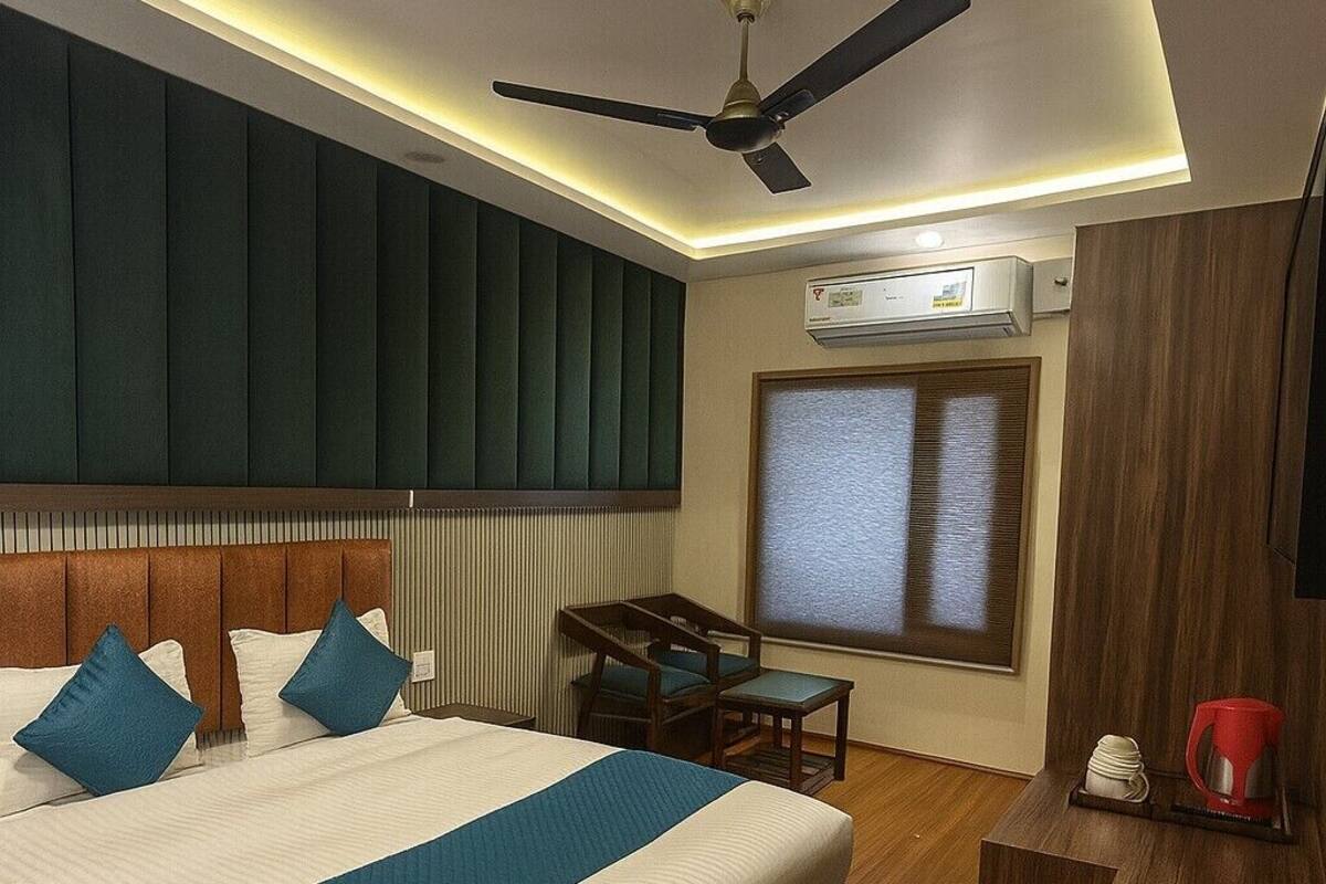 A hotel room with a bed, a desk, a chair, a ceiling fan, an air conditioning unit, and a window.