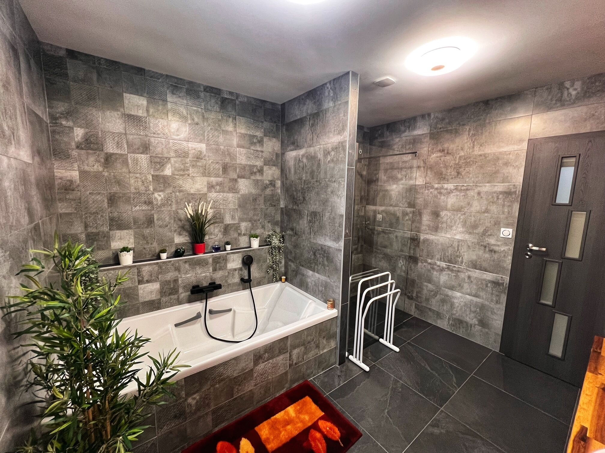 Un baño moderno con bañera, cabina de ducha de vidrio y puerta de madera oscura.