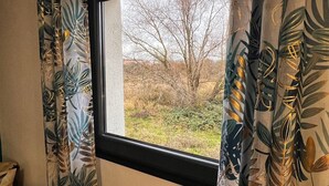 Ett fönster med utsikt över en gardin med ett lövmönster och en enkel vägg.