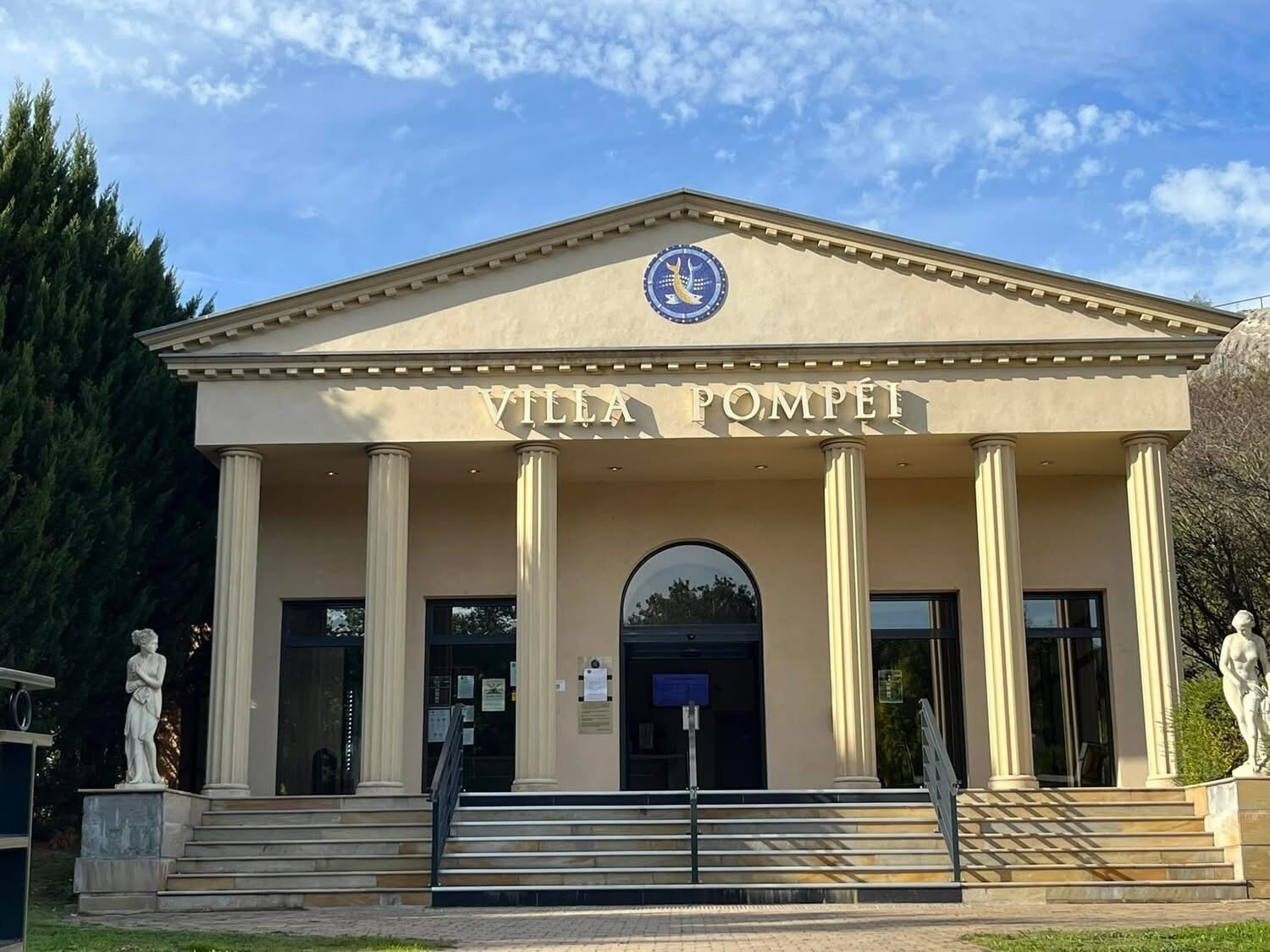 A neoclassical building with the name "Villa Pompeii" on the facade, featuring a central pediment, columns, and statues on either side of the entrance.