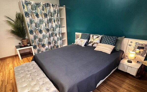 A bedroom with a large bed, a nightstand with a lamp, a small table with a plant, and a curtain with a leaf pattern. - Modern guest room with a bathroom in the new house.   (Maizières-lès-Metz)