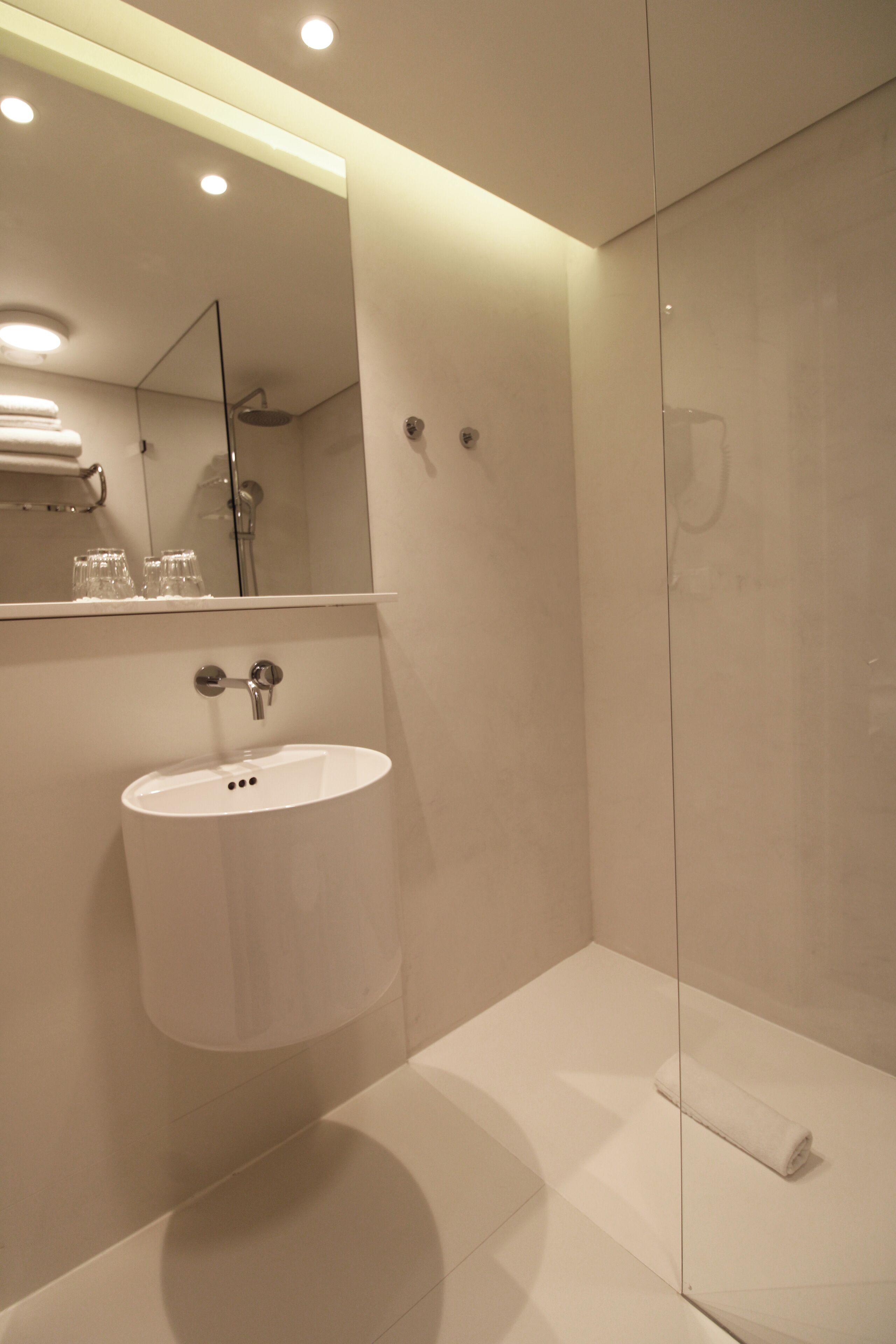 Un baño moderno con un lavabo blanco, una cabina de ducha con mampara de vidrio y un espejo sobre el lavabo.