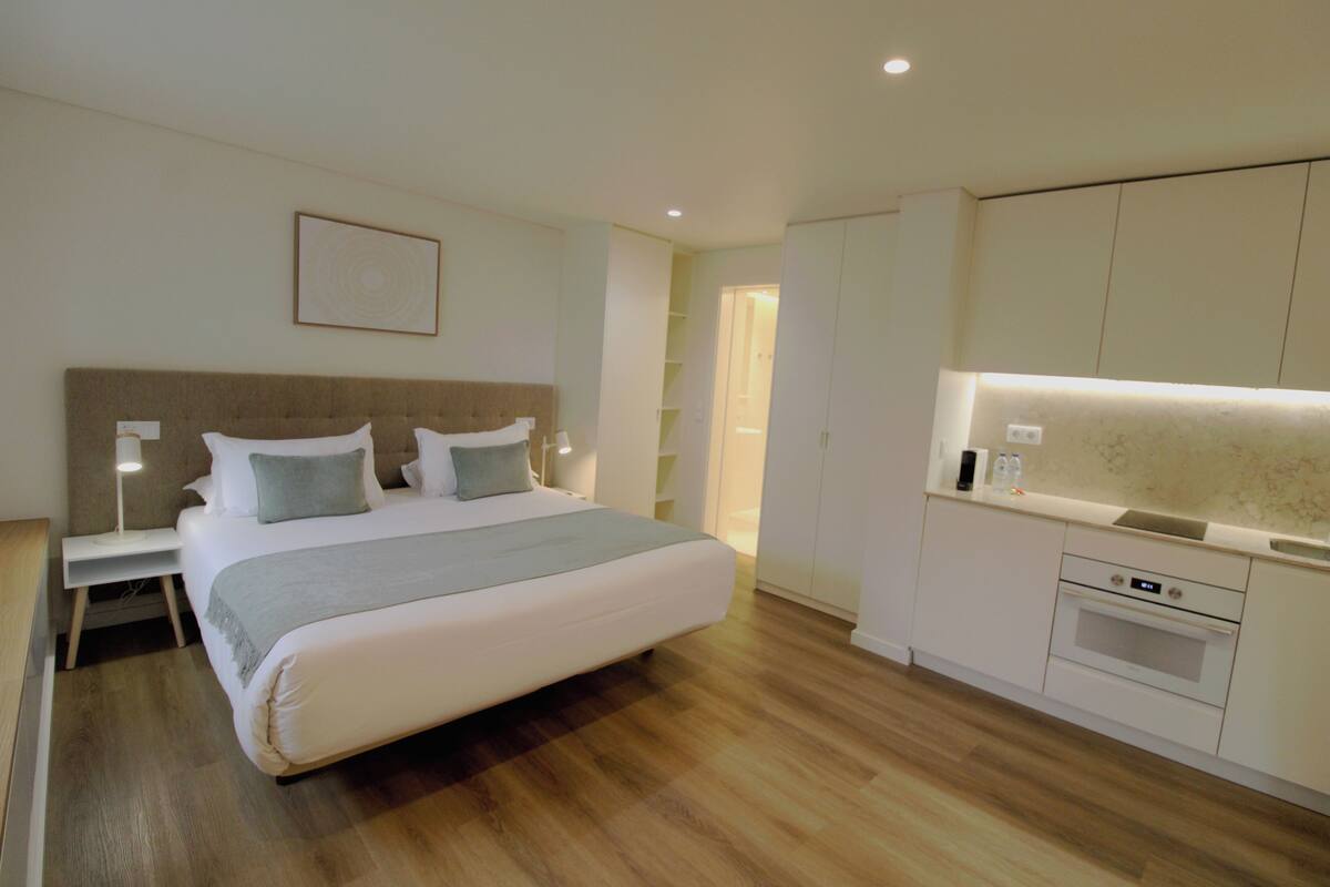 Une chambre moderne avec un grand lit, des tables de chevet, une commode, une armoire intégrée et un coin cuisine.