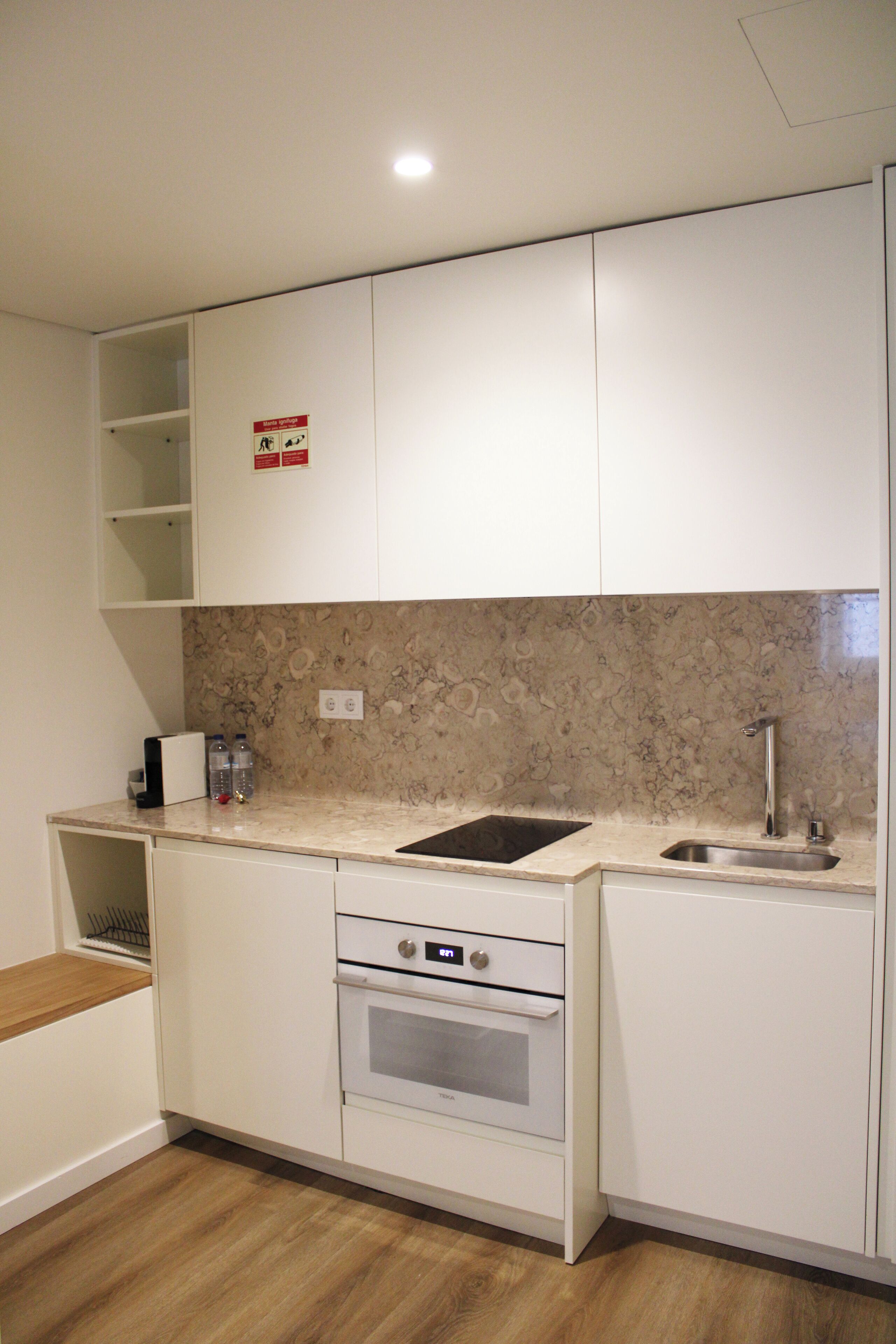 Una cocina moderna con armarios blancos, salpicadero de mármol, horno empotrado y un lavabo.