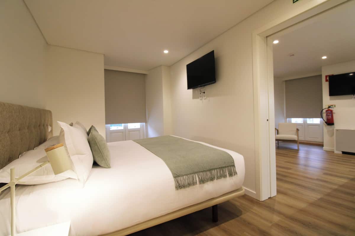 A modern bedroom with a large bed, a flat-screen TV mounted on the wall, and a wooden floor.