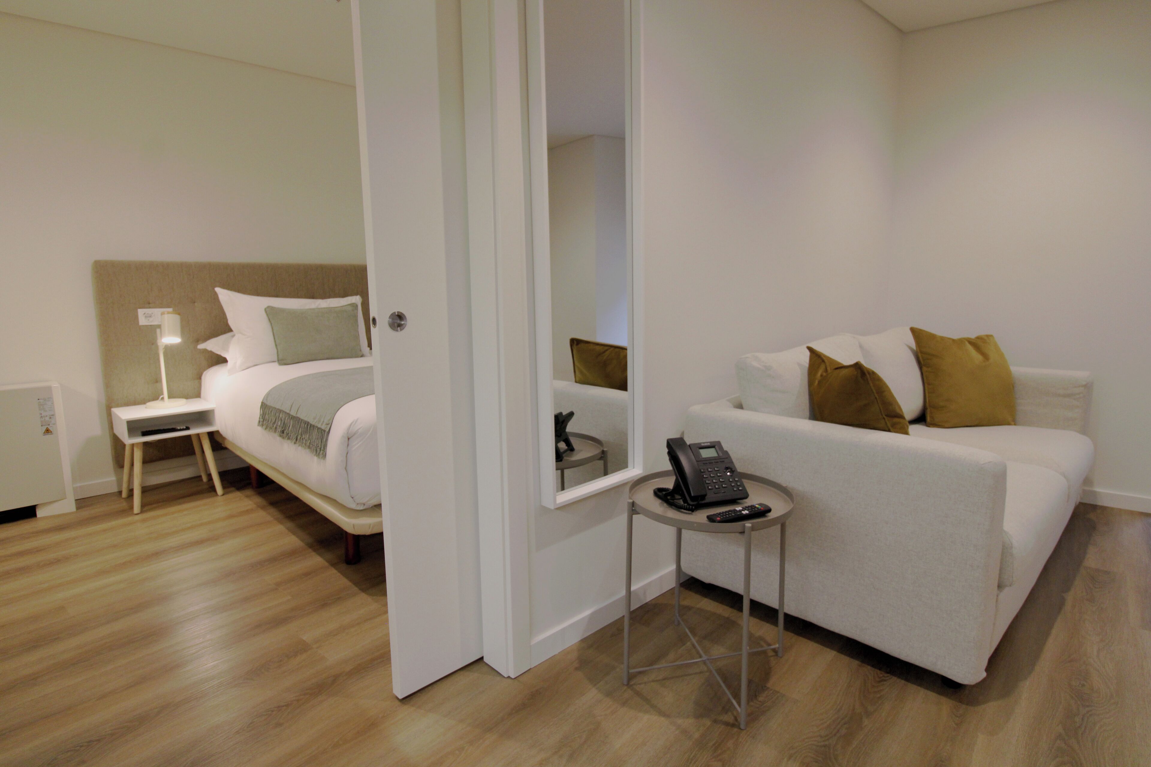 Ein Hotelzimmer mit einem Bett, einem Nachttisch mit Lampe, einem kleinen Beistelltisch mit Telefon und einem Sofa mit Kissen.