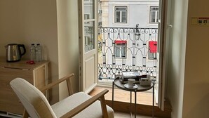 A room with a wooden chair, a small table with a cup, a radiator, and a view of a balcony with a wrought iron gate. - Rossio Garden Suites (Lisbon)