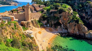 Un pueblo costero con un castillo de piedra histórico, una playa y aguas turquesas cristalinas.