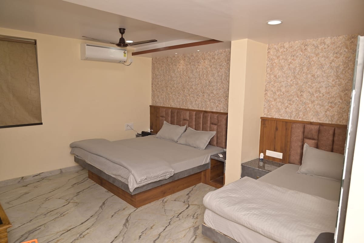 A bedroom with a large bed, a smaller bed, a nightstand, a ceiling fan, and a wall-mounted air conditioner.