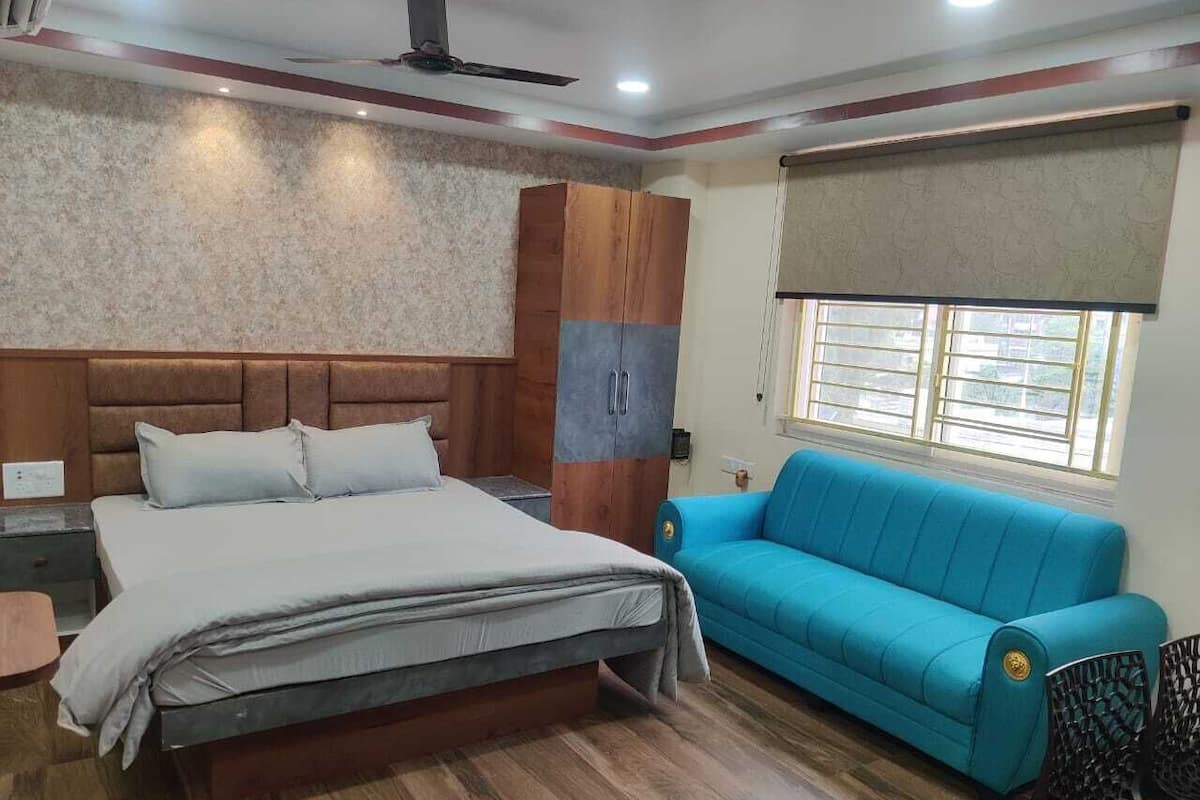 A bedroom with a bed, a blue sofa, a wardrobe, and a window with a curtain.