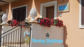 Eine Gebäudefassade mit schmiedeeisernem Tor, dekorativen Vasen und einem Schild mit der Aufschrift 'Navian Holidays Giardini Naxos'.