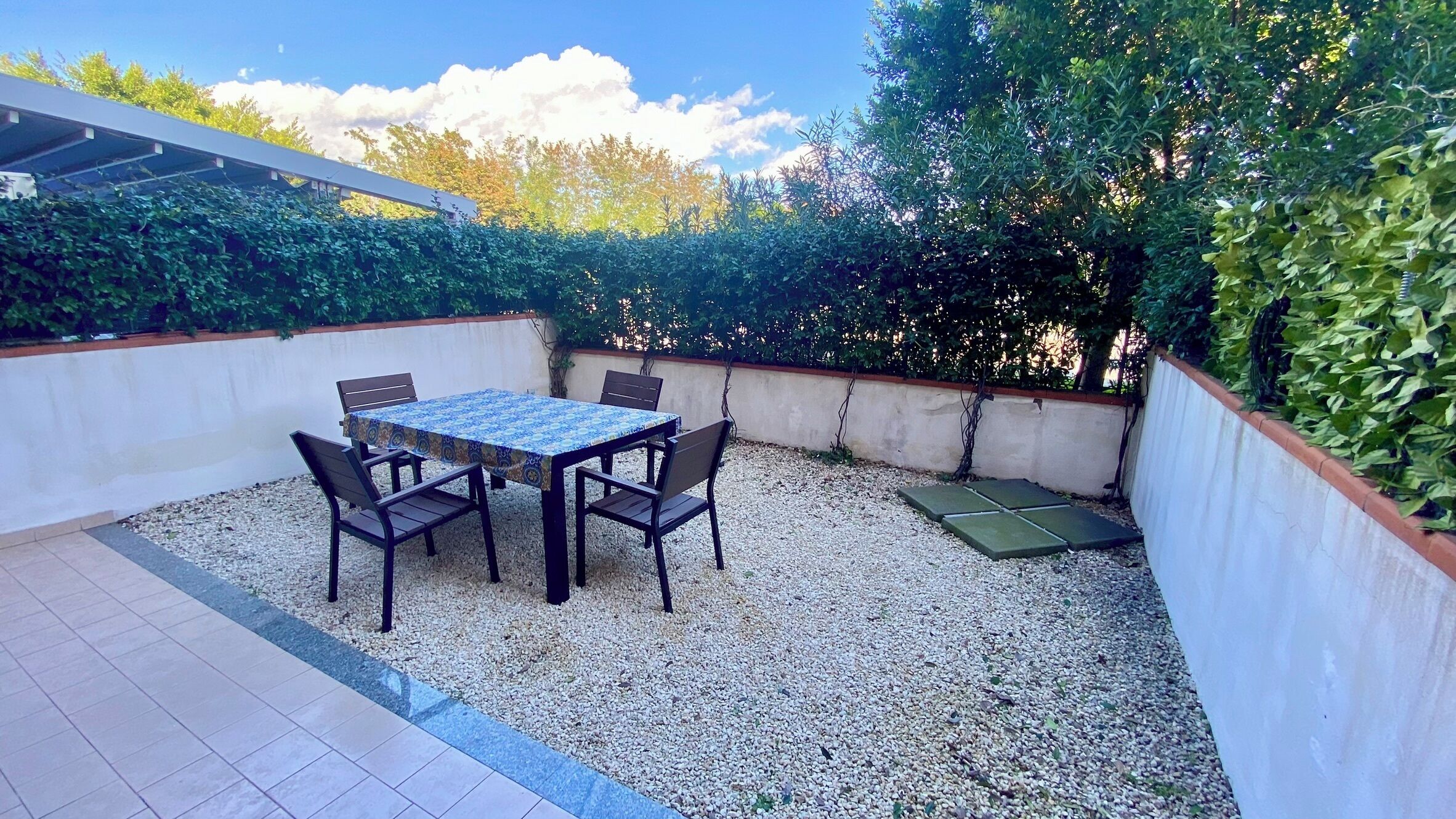 A patio with a table and chairs, surrounded by gravel and a low wall.