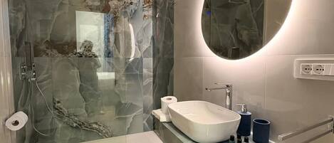 A modern bathroom with a glass-enclosed shower, a freestanding sink, and a vanity with a mirror.