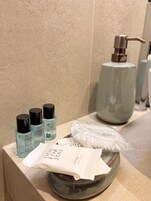 Una encimera de baño con artículos de aseo, incluyendo un dispensador de jabón, productos para el cabello y una bolsa de plástico.