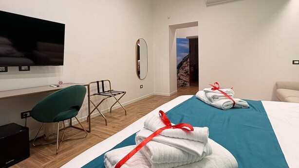 A hotel room with a bed, a desk, a chair, a TV, and a bathroom visible through an open door. - Alla Scoperta di Napoli (Naples)