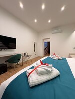 Habitación de hotel con cama, escritorio, silla, televisor y baño visible a través de una puerta abierta.