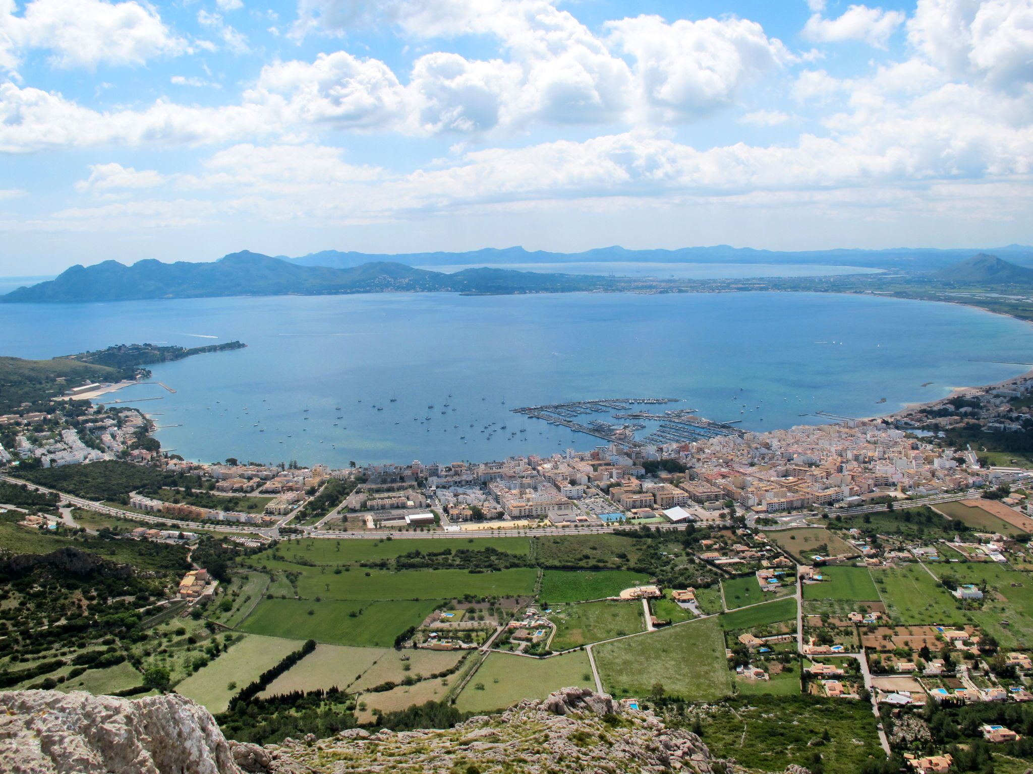 A coastal town with a marina, green fields, and a mountainous backdrop.
