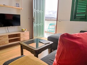 Ein Zimmer mit Fernseher, Holzmöbeln, einem Glastisch, einer Couch und einer Tür, die auf einen Balkon führt.
