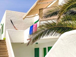 Ein weißes Gebäude mit grünen Fensterläden, einer Treppe und einer Palme.