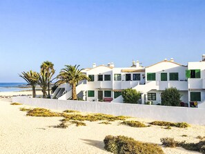 Ein Hotel direkt am Strand mit weißen Gebäuden, grünen Fensterläden und Palmen.