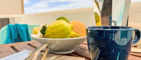 A table with a blue mug, a white bowl with fruit, and a book titled 'Der Fischer'.