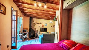 Een slaapkamer met een houten plafond, een bed met rode beddengoed, een televisie en een open haard.