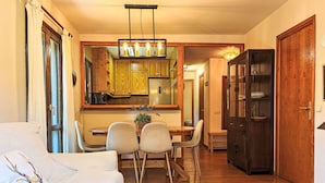A living room with a sofa, a dining table with chairs, a kitchen area with wooden cabinets, and a hallway.