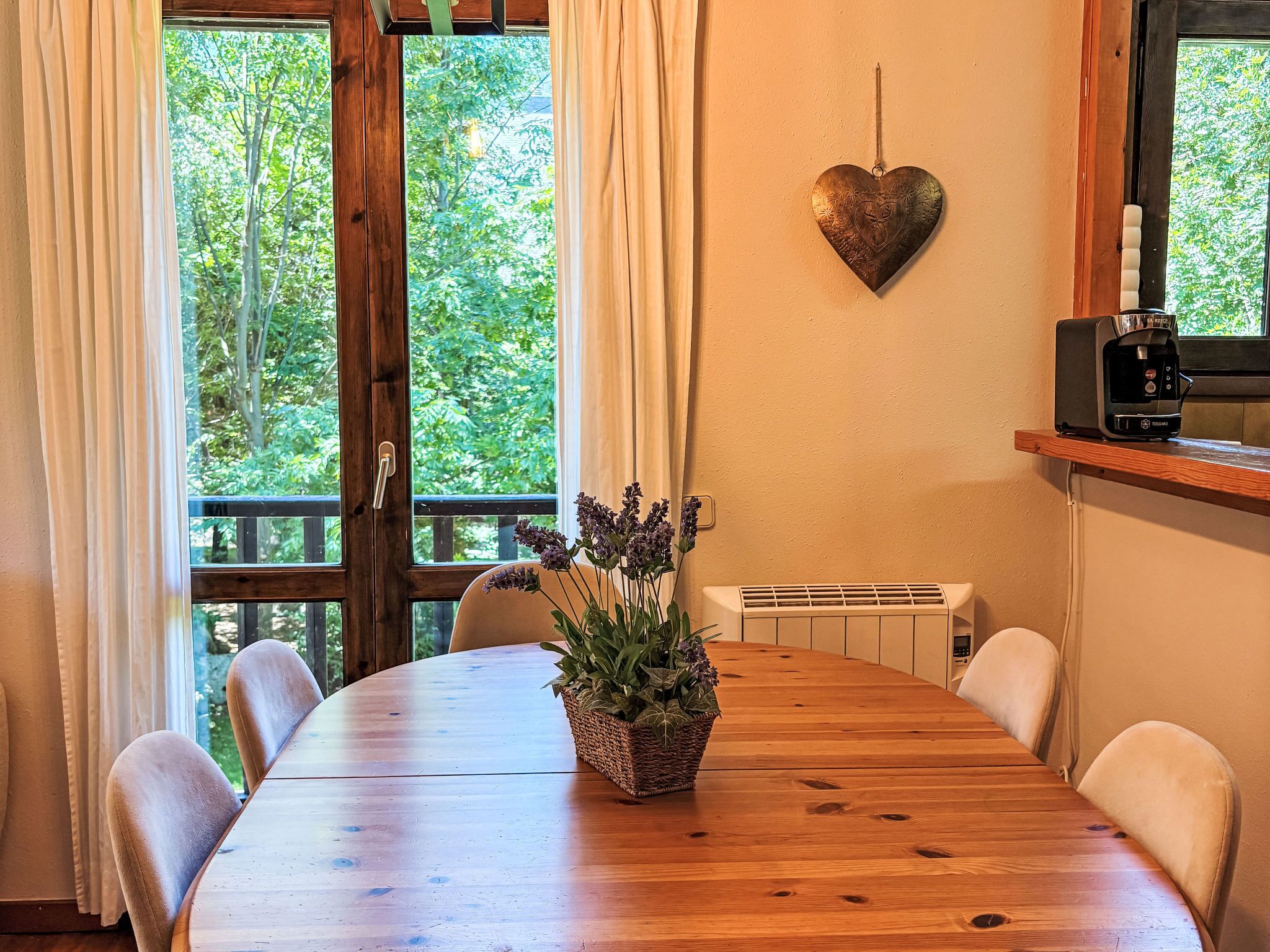 Une table à manger en bois avec des chaises, une décoration en forme de cœur, une plante et une machine à café.