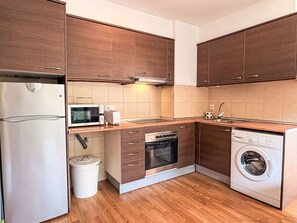 Eine moderne Küche mit Holzschränken, einem Kühlschrank, einer Mikrowelle, einem Geschirrspüler, einem Backofen und einer Waschmaschine.