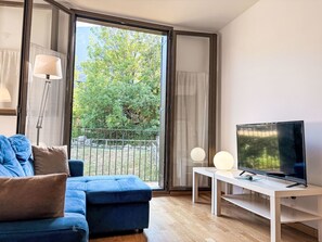 A modern living room with a blue sofa, a TV on a white stand, and a view of greenery through large sliding doors. - Gemütliche und komfortable Wohnung Aüt 2 Vall de Boí by Interhome (Caldes de Boi)