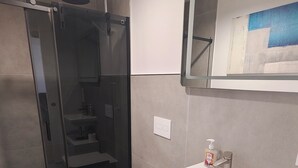 Un baño moderno con cabina de ducha de vidrio, un lavamanos blanco con espejo y un inodoro.