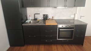 Una cocina compacta con refrigerador, pileta, cocina y gabinetes oscuros.