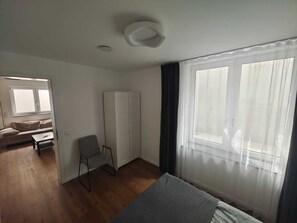 Ein Zimmer mit einem Bett, einem Sessel, einem Sofa, einem Kleiderschrank und einem fensterbelaubten Fenster.