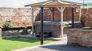 Um gazebo com hidromassagem, cercado por um muro de pedra e um gramado.