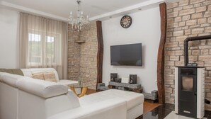 A modern living room with a white sofa, a glass coffee table, a fireplace, and a flat-screen TV mounted on a stone wall. - Cozy Villa for 8 with Pool and Jacuzzi (Šumet)