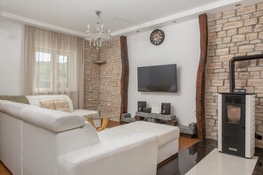 Ein modernes Wohnzimmer mit einem weißen Sofa, einem Glastisch, einem Kamin und einem Flachbildfernseher, der an einer Steinwand angebracht ist.