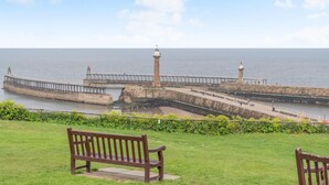Vista costeira com um farol, cais e área gramada com bancos.