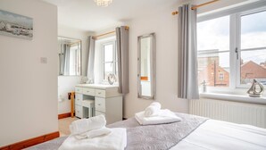 Quarto com cama, penteadeira, espelho e janela com vista para edifícios.