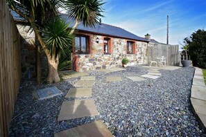 A stone house with a red roof, a gravel driveway, and a palm tree. - 2 Bed in Pwllheli (oc-nythyw) (Llanengan)