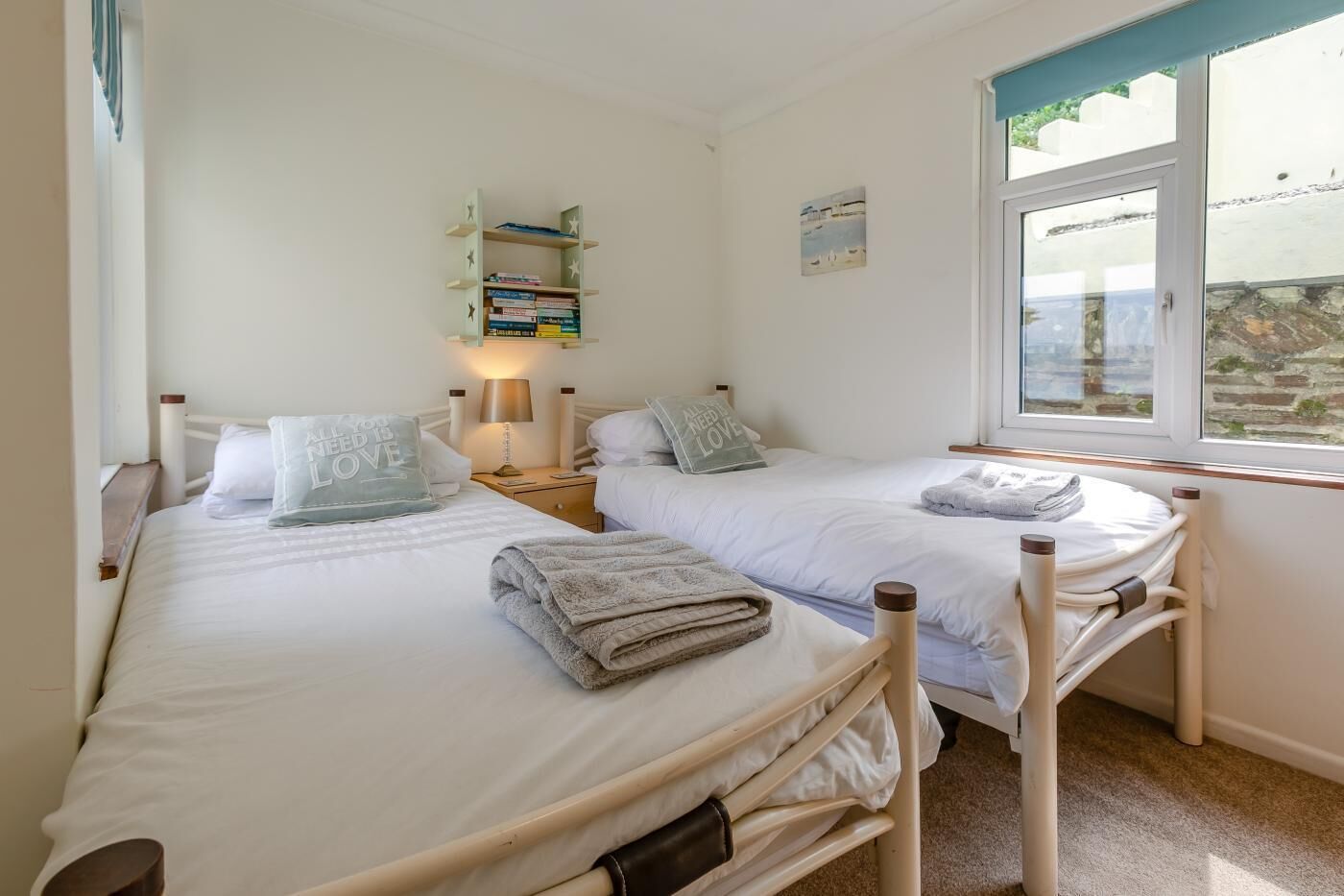 A twin room with two beds, a nightstand, a lamp, a bookshelf, and a window with a view.